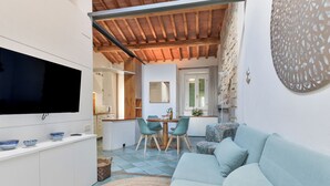 A modern kitchen with a dining area, a TV mounted on the wall, and a light blue sofa. - Agriresort Galenzana (Campo nell'Elba)