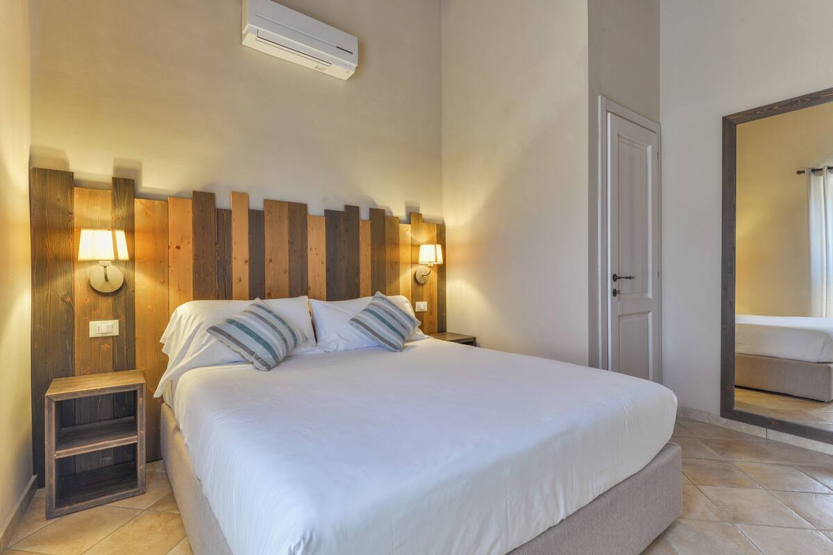 A bedroom with a wooden headboard, two bedside lamps, a nightstand, and a large bed with pillows.