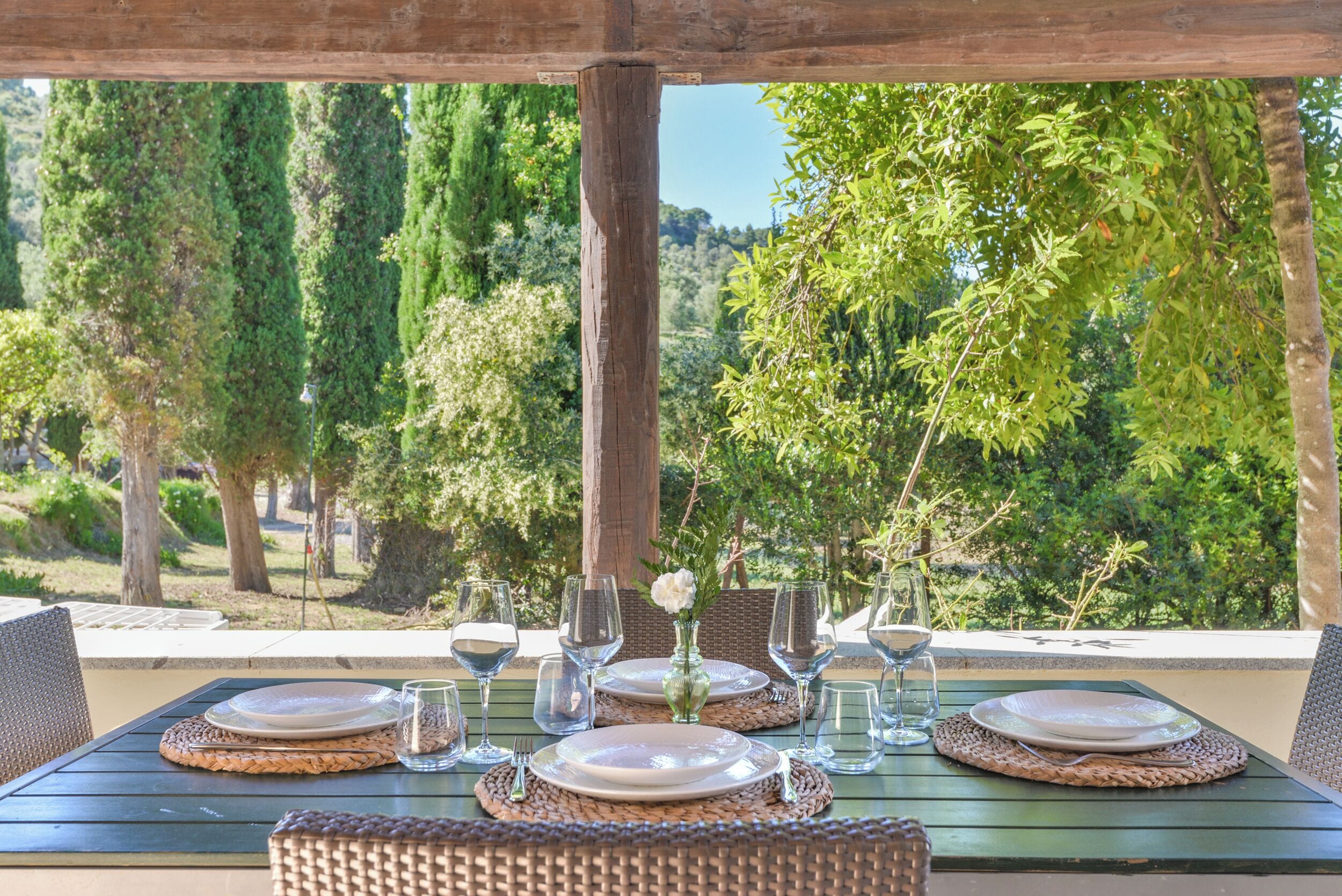 An outdoor dining area with a table set for four, surrounded by greenery and trees.