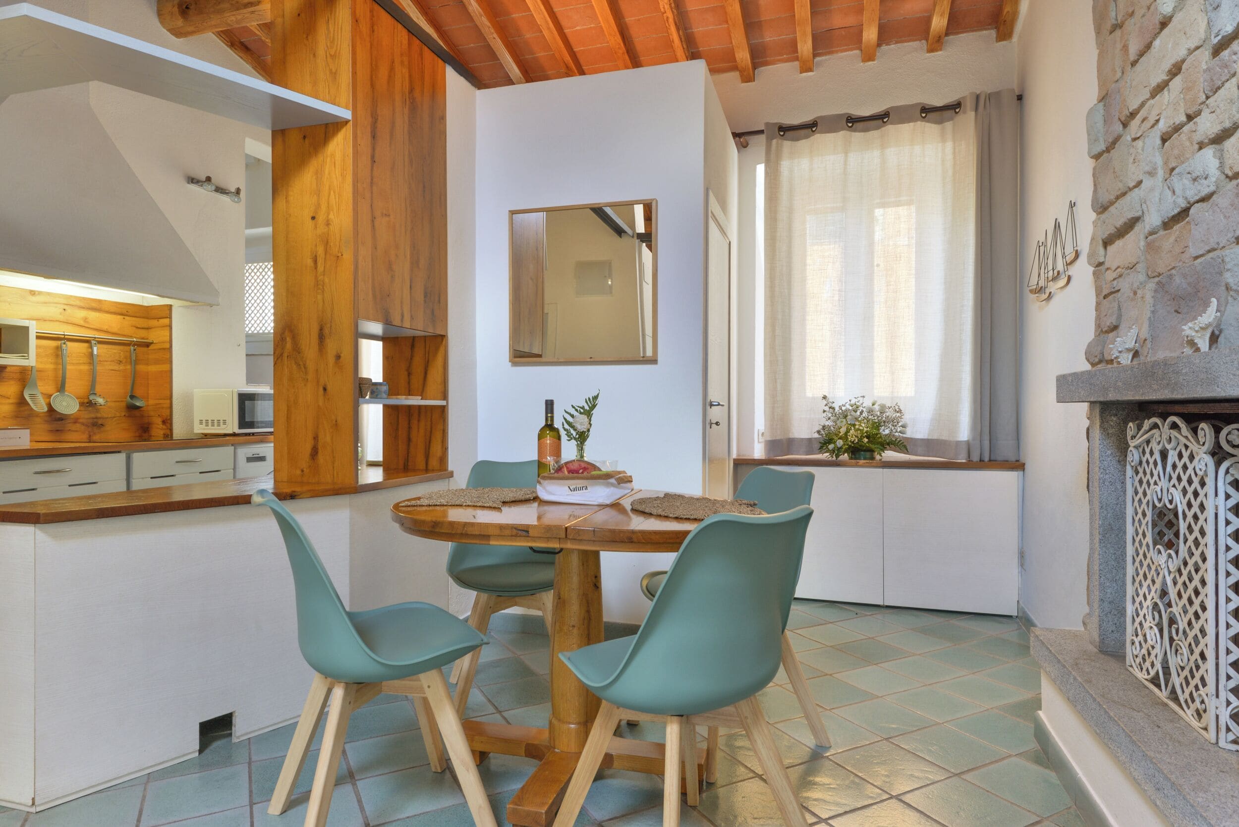 Une cuisine avec des meubles en bois, une table à manger avec des chaises, un miroir et une fenêtre avec des rideaux.
