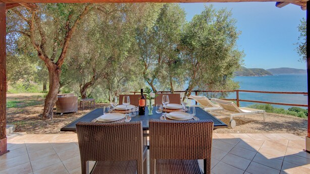 An outdoor dining area with wicker furniture, a table set for four, and a view of the sea. - Agriresort Galenzana (Campo nell'Elba)