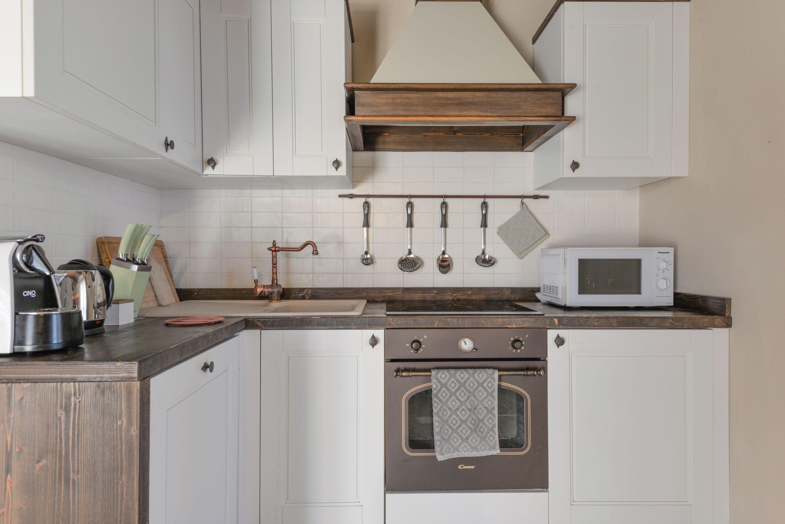 Una cocina con alacenas blancas, encimera de madera, estufa, microondas y utensilios colgantes.