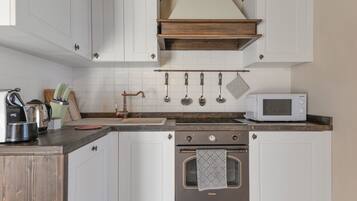 Una cocina con alacenas blancas, encimera de madera, estufa, microondas y utensilios colgantes.
