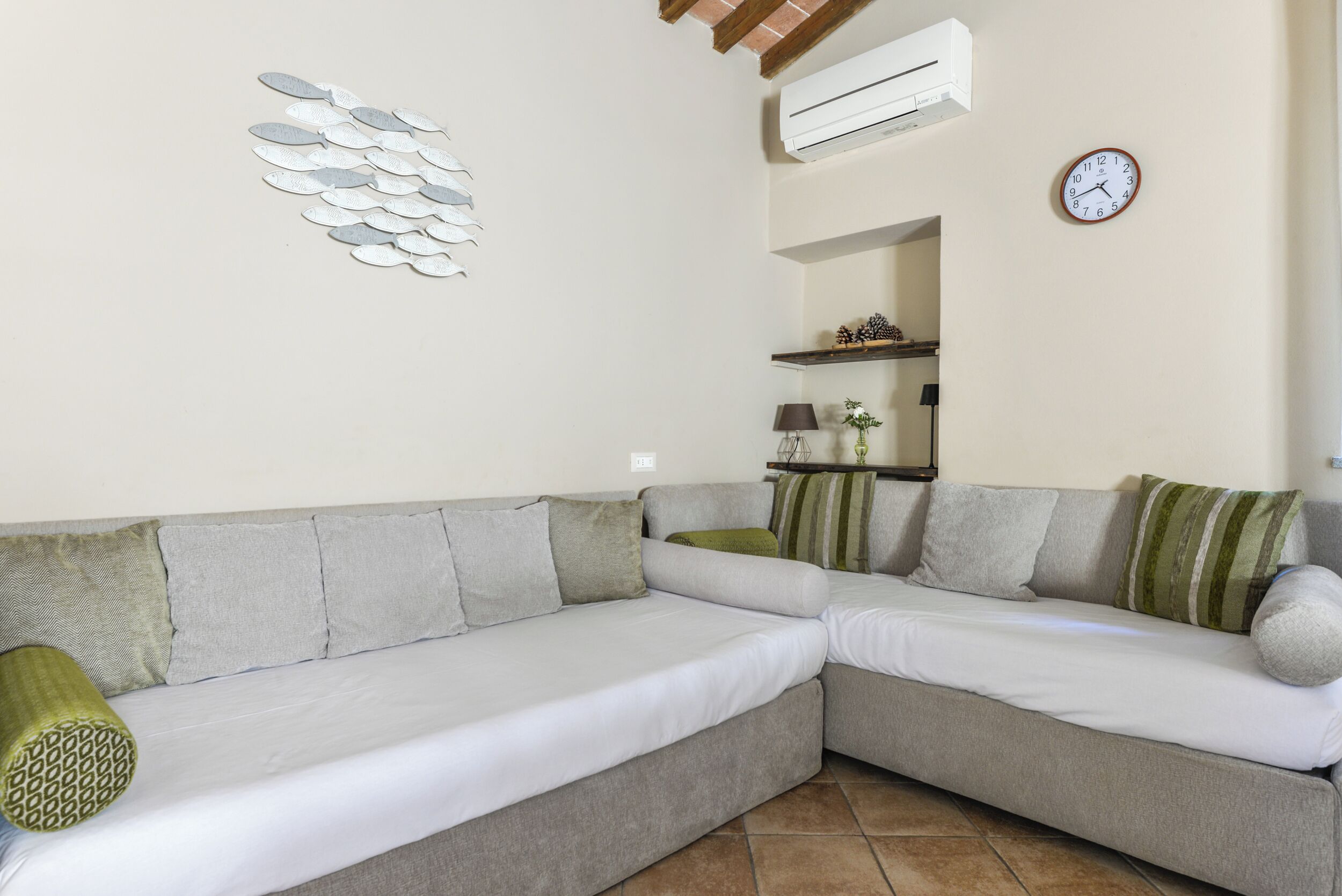 Una sala de estar moderna con un sofá modular, un reloj en la pared y un equipo de aire acondicionado.