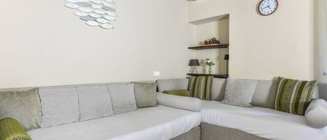 Una sala de estar moderna con un sofá modular, un reloj en la pared y un equipo de aire acondicionado.
