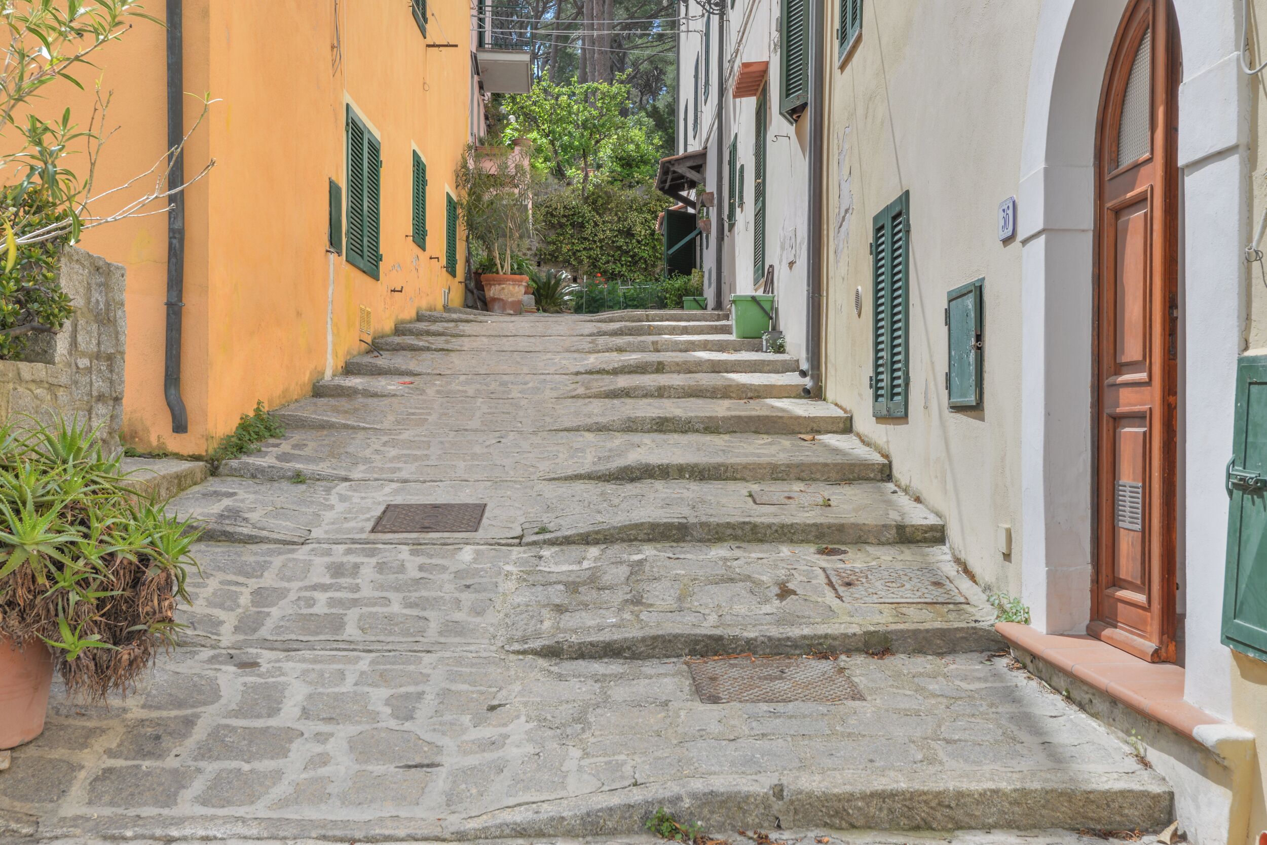 A narrow stone staircase leading up to a building with green shutters and a wooden door.