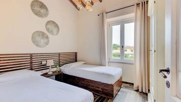 Un dormitorio con dos camas, cabeceros de madera, una mesita de noche con lámpara y una ventana con cortinas.