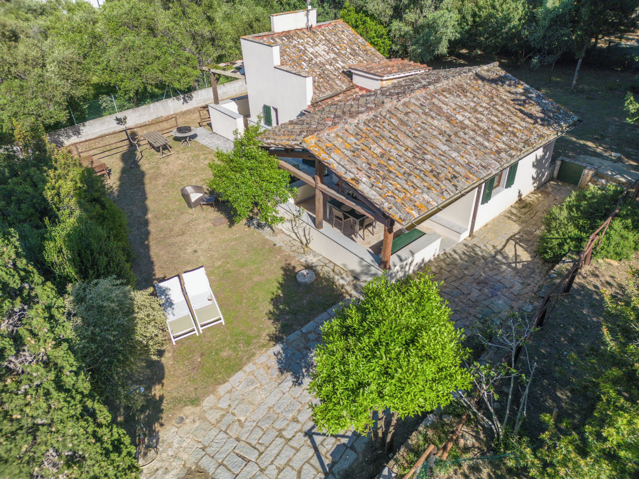 Una casa de dos pisos con techo de tejas, un patio con mobiliario exterior y un jardín.