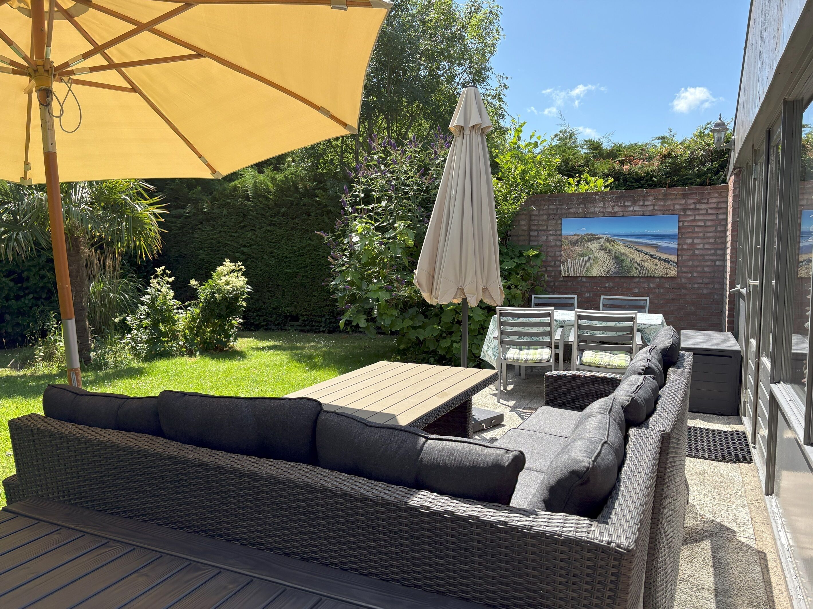 Une terrasse extérieure aménagée avec des meubles en osier, une table en bois et deux parasols.