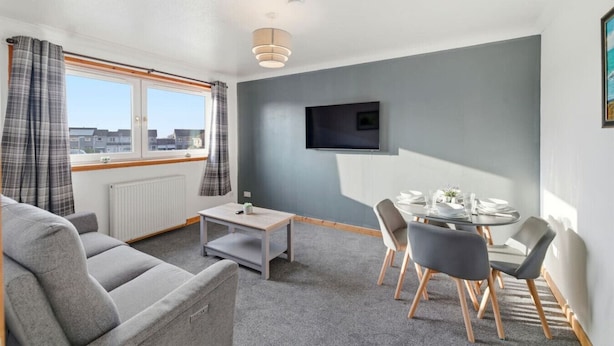 Ein modernes Wohnzimmer mit grauem Sofa, einem kleinen Tisch und einem Essbereich mit rundem Tisch und Stühlen.