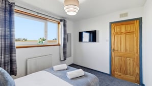 Ein Hotelzimmer mit Bett, Fernseher, Holztür und einem Fenster mit Vorhängen.