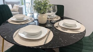A round dining table with white plates, cutlery, and a woven placemat. There is a vase with green foliage and two wine glasses on the table. - Albert Dock Luxury Penthouse – Walk to Liverpool ONE (Liverpool)