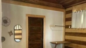 Una stanza con pareti in legno, un letto con copriletto bianco, un tavolino, uno specchio e una lampada a sospensione.