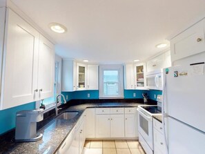 A modern kitchen with white cabinets, a black countertop, a built-in oven, and a refrigerator. - Charming House Near the Beach | Porch, Deck & BBQ (Bethany Beach)