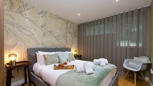 A modern bedroom with a bed, bedside tables, a chair, and a wall mural. - Karolva, St Ives - Ground Floor Apartment – On -Site Parking (St Ives)
