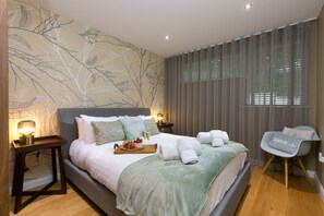 A modern bedroom with a bed, bedside tables, a chair, and a wall mural. - Karolva-St Ives-Ground Floor Apartment-Parking (St Ives)