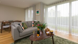 A living room with a sofa, coffee table, and dining table. - Karolva, St Ives - Ground Floor Apartment – On -Site Parking (St Ives)