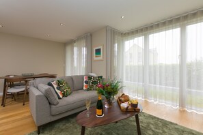A living room with a sofa, coffee table, and dining table. - Karolva-St Ives-Ground Floor Apartment-Parking (St Ives)