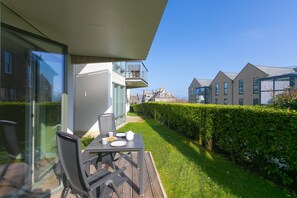 A modern outdoor dining area with a table and chairs, a glass door, and a view of neighboring houses. - Karolva-St Ives-Ground Floor Apartment-Parking (St Ives)
