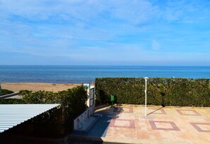 Blick auf einen Strand vom Balkon aus, mit Fliesenboden, einer grünen Mülltonne und einem weißen Lampenpfahl.
