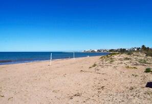 Ein Strand mit Volleyballnetz, blauem Himmel und einer fernen Küstenlinie mit Gebäuden.