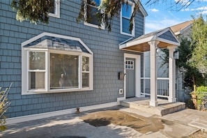 A house with a grey siding exterior, a front porch with a white railing, and a window with blinds.