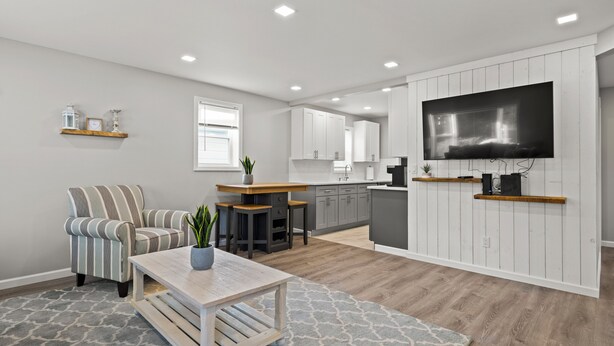 A modern kitchen with white cabinets, a wooden countertop, and a large TV mounted on the wall.