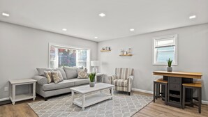 A modern living room with a grey sofa, a coffee table, a striped armchair, and a wooden desk with shelves.