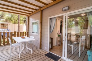 Ein überdachter Außenbereich mit Tisch und Stühlen, ein Holzdeck und eine Glastür zu einem Innenraum mit Esstisch und Stühlen.