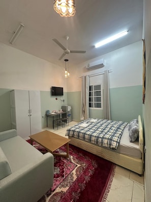 Une chambre à coucher comprenant un lit, un bureau, une chaise, une armoire et un ventilateur de plafond.