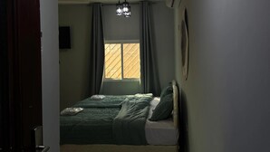 A bedroom with a bed, a window with curtains, a ceiling light fixture, and an air conditioning unit.
