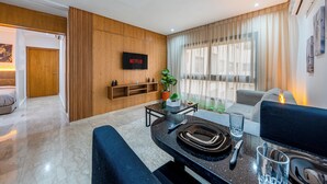 Ein modernes Wohnzimmer mit Essbereich, einem montierten Fernseher, der 'NETFLIX' anzeigt, einer Topfpflanze und einem Sofa.