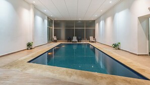Ein Hallenbad mit gefliestem Boden, klarem, blauem Wasser und mehreren Liegestühlen.