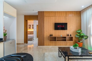 A modern living room with a flat-screen TV mounted on a wooden wall, a marble coffee table, and a small potted plant. - Le Grand Chic - Downtown swimming pool (Marrakesh)