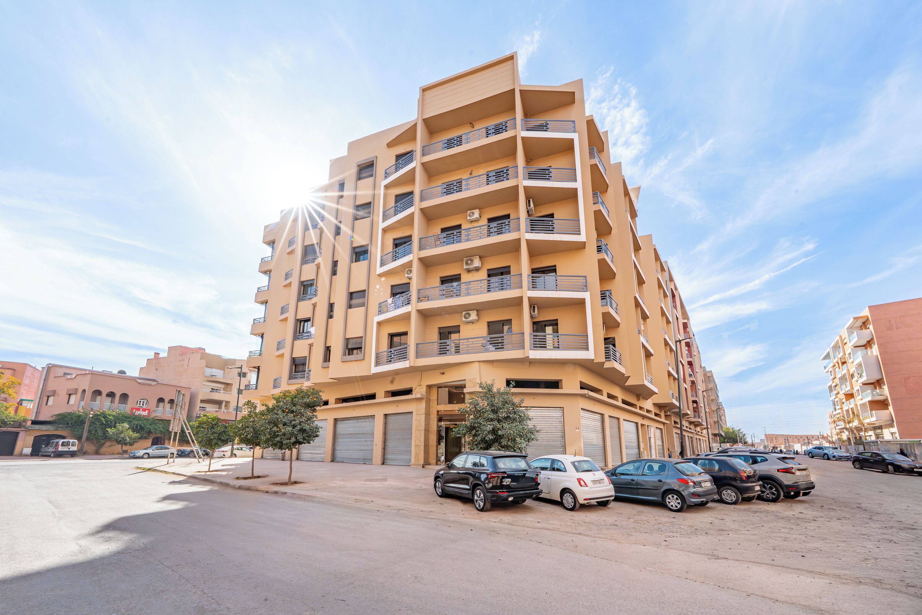 Un edificio residencial de varios pisos con balcones, un estacionamiento y cielo despejado.