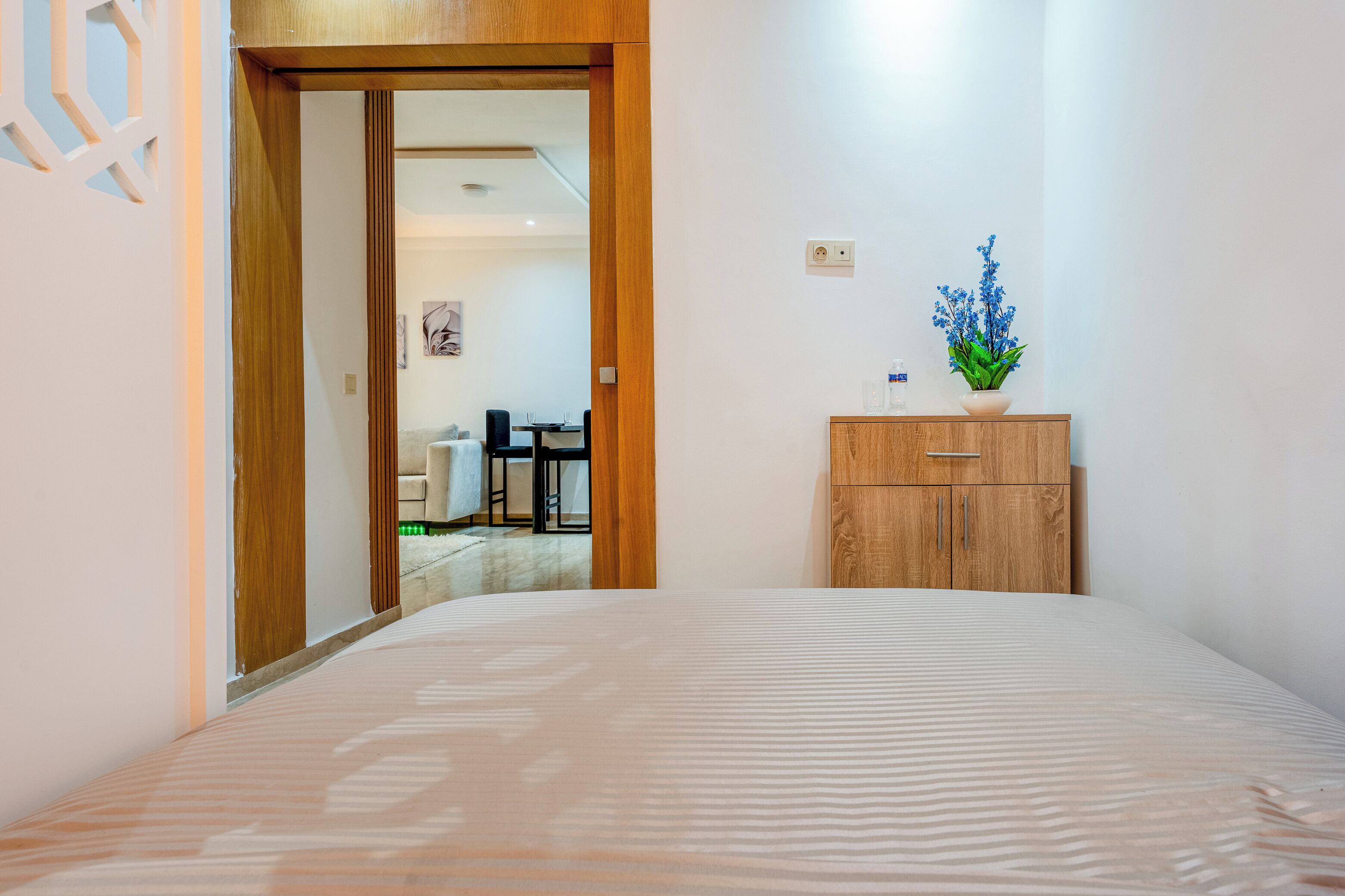 Une chambre d’hôtel avec un lit, une armoire en bois ornée d’une plante, et donnant sur la salle à manger.