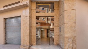 Ein modernes Gebäude mit Eingang, geschlossenem Garagentor, einem Glaselevator und einem sichtbaren Auto darin.