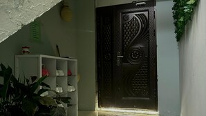 A staircase leading to a room with a decorative door, a white shelf unit, and a potted plant.