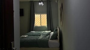 A bedroom with a bed, a window with curtains, a ceiling light fixture, and an air conditioning unit.