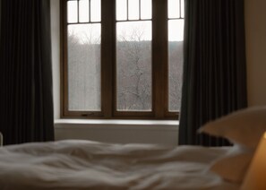 Een bed met uitzicht op een bevroren landschap door een raam met gordijnen.