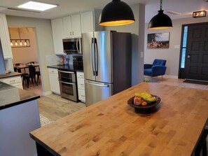 Une cuisine moderne dotée d’appareils électroménagers en acier inoxydable, d’un îlot central en bois et de luminaires suspendus.