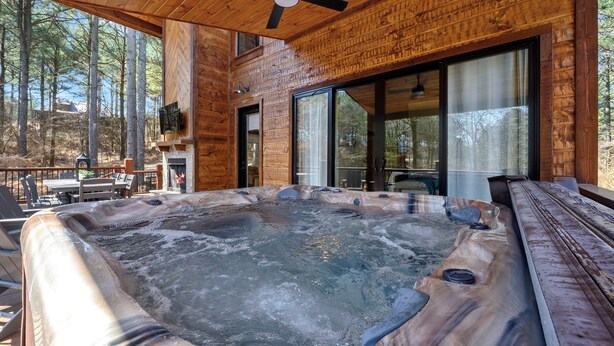Una cabaña de madera con jacuzzi, ventanas amplias y un ventilador de techo.