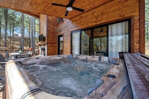 A wooden cabin with a hot tub, large windows, and a ceiling fan.