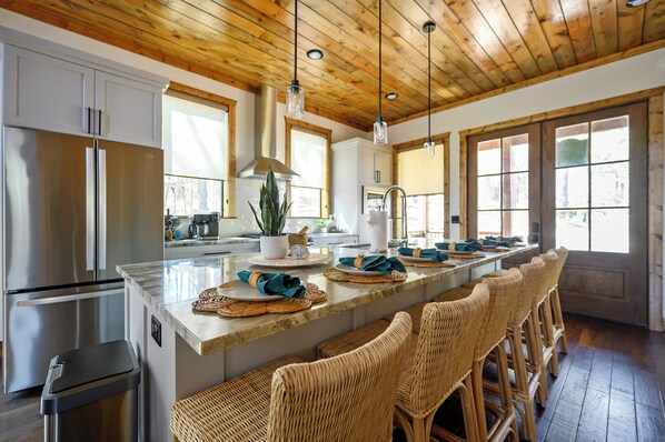 A modern kitchen with a central island, stainless steel appliances, and wicker bar stools.