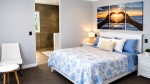 A bedroom with a bed, nightstands, a chair, a ceiling fan, and a wall with a sunset painting.
