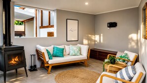 A living room with a fireplace, a sofa, a chair, a woven rug, and a window overlooking a balcony.