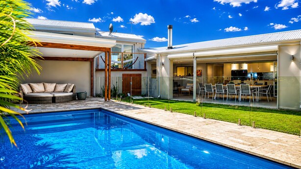 A modern house with a swimming pool, outdoor seating, and a glass-enclosed dining area.