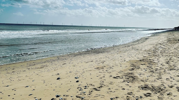 A beach with footprints and shells, a clear sky, and wind turbines in the distance. - Traditional 1850s fisherman’s cottage, perfect coastal retreat, sea views. (Scratby)