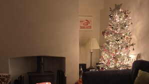 A cozy living room with a fireplace, a Christmas tree, and a dark-colored sofa. - Traditional 1850s fisherman’s cottage, perfect coastal retreat, sea views. (Scratby)