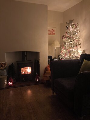 A cozy living room with a fireplace, a Christmas tree, and a dark-colored sofa. - Traditional 1850s fisherman’s cottage, perfect coastal retreat, sea views. (Scratby)